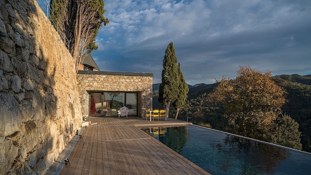 A stone building with a wooden deck leading to a swimming pool.
