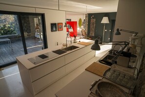 A modern kitchen with a large island, a dining area with a red chair, and a view of a patio.