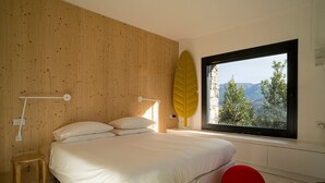 A bedroom with a bed, a window with a view, a bedside lamp, and a wooden wall.