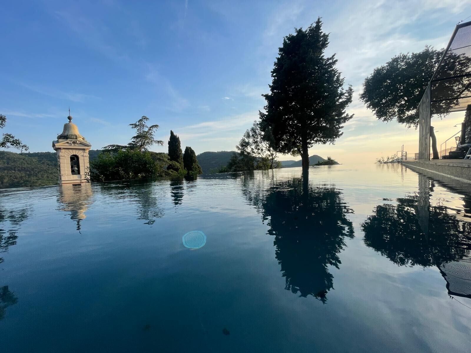A serene outdoor pool area with a bell tower, surrounded by trees and a clear sky.