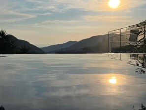A tranquil outdoor pool area with a clear view of the surrounding hills and a sunset in the background.
