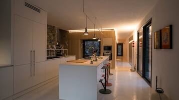 Een moderne keuken met een centraal eiland, hangende verlichting en uitzicht op de eethoek.
