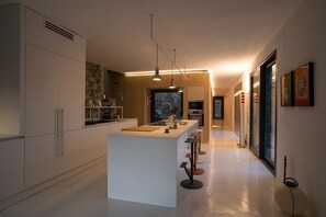 A modern kitchen with a central island, pendant lighting, and a view into the dining area.