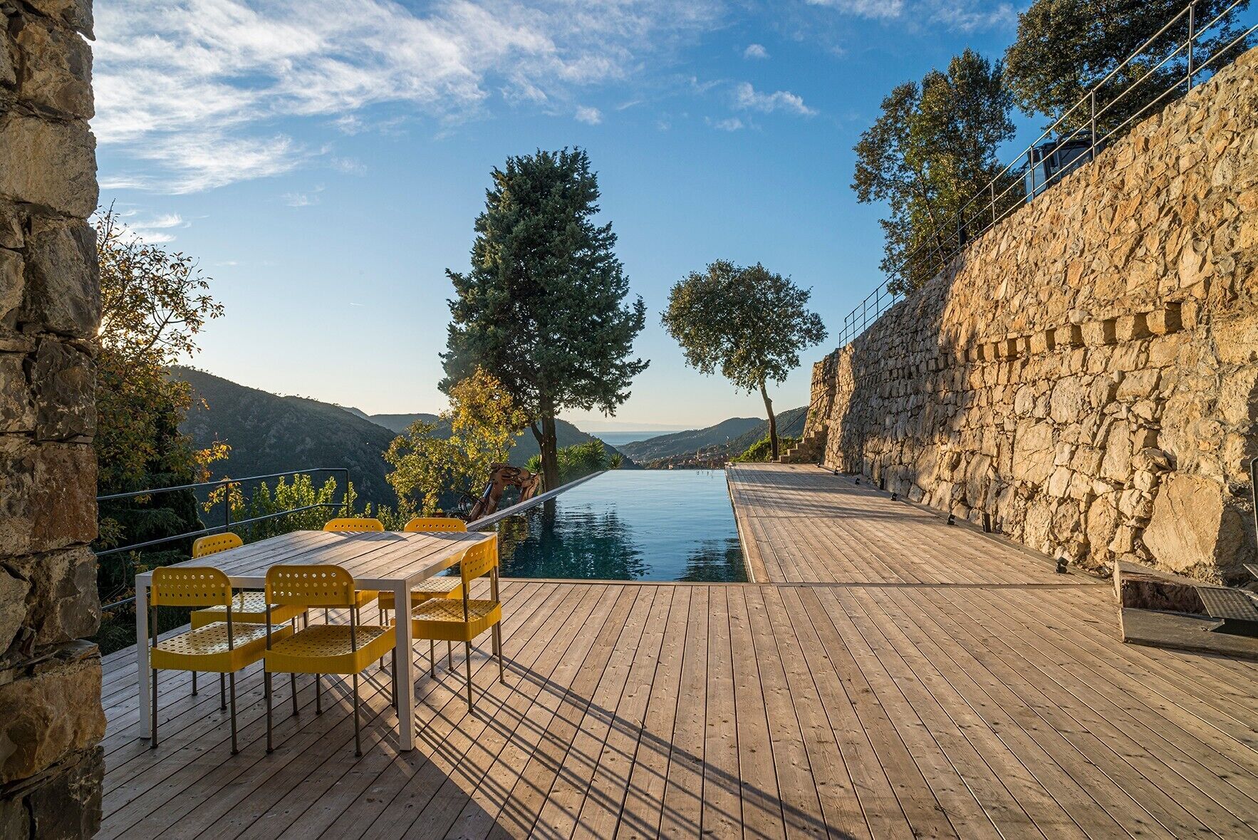 A wooden deck with a pool, stone walls, and a view of the mountains.