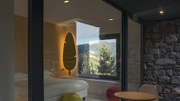 Une chambre moderne avec un grand lit, un mur en verre et une vue sur un paysage montagneux.