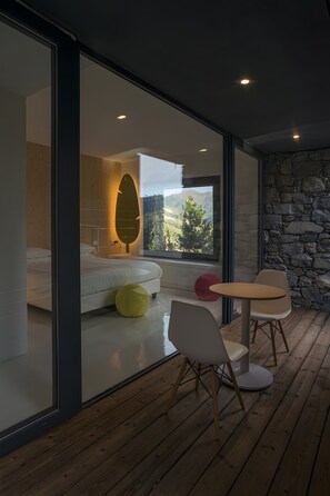 A modern bedroom with a large bed, a glass wall, and a view of a mountainous landscape.
