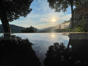 A serene outdoor pool area with a clear view of the sun setting behind a mountain range.