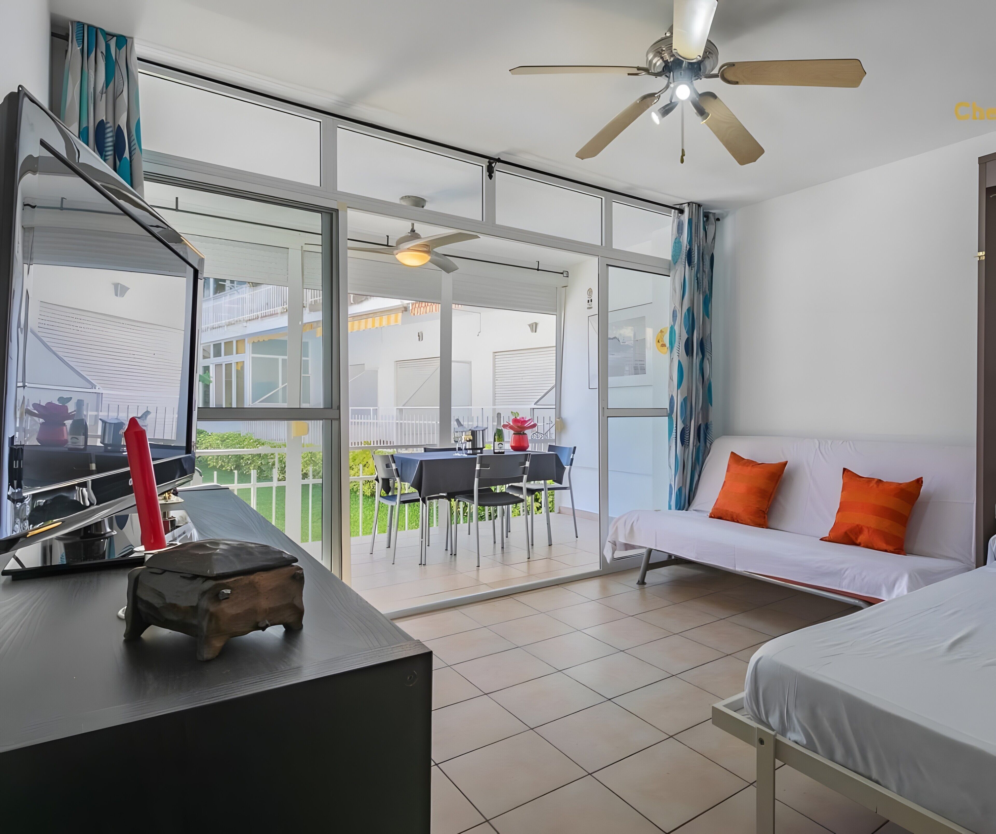 Ein modernes Hotelzimmer mit Balkon, einer Couch mit orangefarbenen Kissen, einem Bett und einem Schreibtisch mit roter Vase.