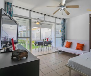 Una habitación de hotel moderna con balcón, un sofá con cojines naranja, una cama y un escritorio con un jarrón rojo.