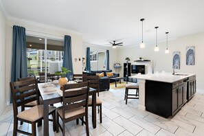 A modern kitchen with a central island, dining area with wooden chairs and a table, and a living area with a sofa and coffee table. - Last Minute Disney Getaway! Private Pool & Themed Bedrooms. Book Now! #107643 (Orlando)