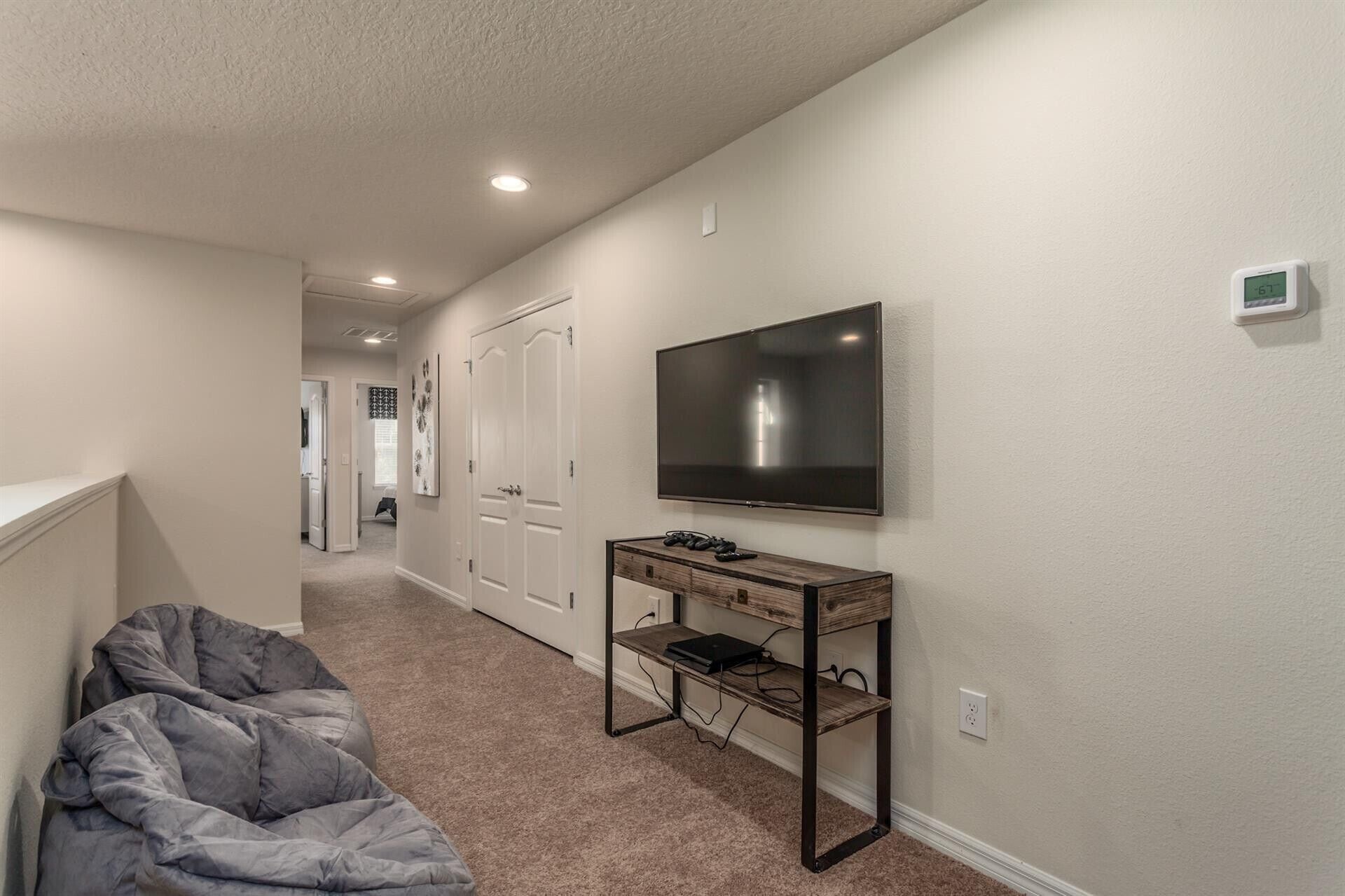 A hallway with a flat-screen TV mounted on the wall, a wooden console table with electronic devices, and a gray couch.