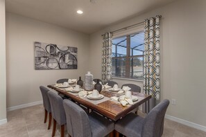 A dining area with a wooden table set for four, grey upholstered chairs, a large abstract painting on the wall, and patterned curtains over a window. - Last Minute Disney! Private Pool, Hot Tub & Themed Bedrooms. Book Now! #107657 (Orlando)
