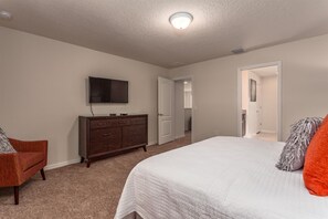 Un dormitorio con cama, cómoda, televisor y una puerta que da a otra habitación.