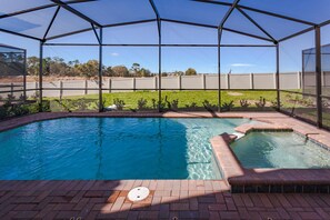 Una piscina con jacuzzi integrado, rodeada por una zona cubierta con vistas a un campo de césped y una cerca.