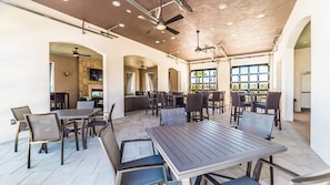 A spacious outdoor dining area with multiple tables and chairs, a ceiling fan, and a stone wall in the background. - Last Minute Disney! Private Pool, Hot Tub & Themed Bedrooms. Book Now! #107657 (Orlando)
