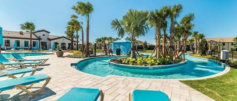 Un área de piscina con sillones de descanso, palmeras y una carpa azul.