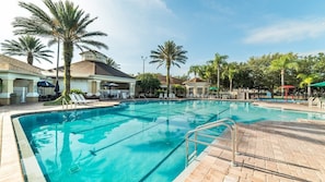 Ein Pool mit Liegestühlen, Palmen und einem Gebäude mit hellblauer Fassade.