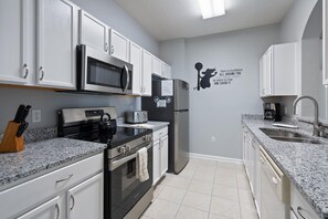 A modern kitchen with white cabinets, stainless steel appliances, a granite countertop, and a wall decal. - Last Minute Disney Getaway! Luxury Condo with Private Balcony. Book Now! #108399 (Orlando)