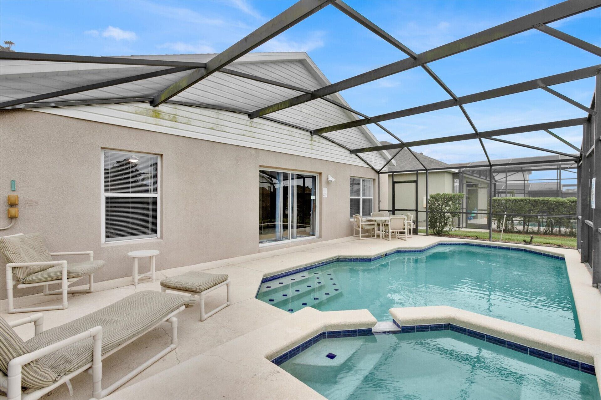 A covered outdoor swimming pool area with lounge chairs and a patio table.