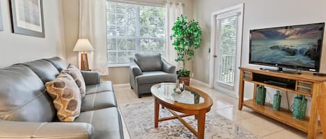 A living room with a sofa, armchair, coffee table, TV, and a potted plant.