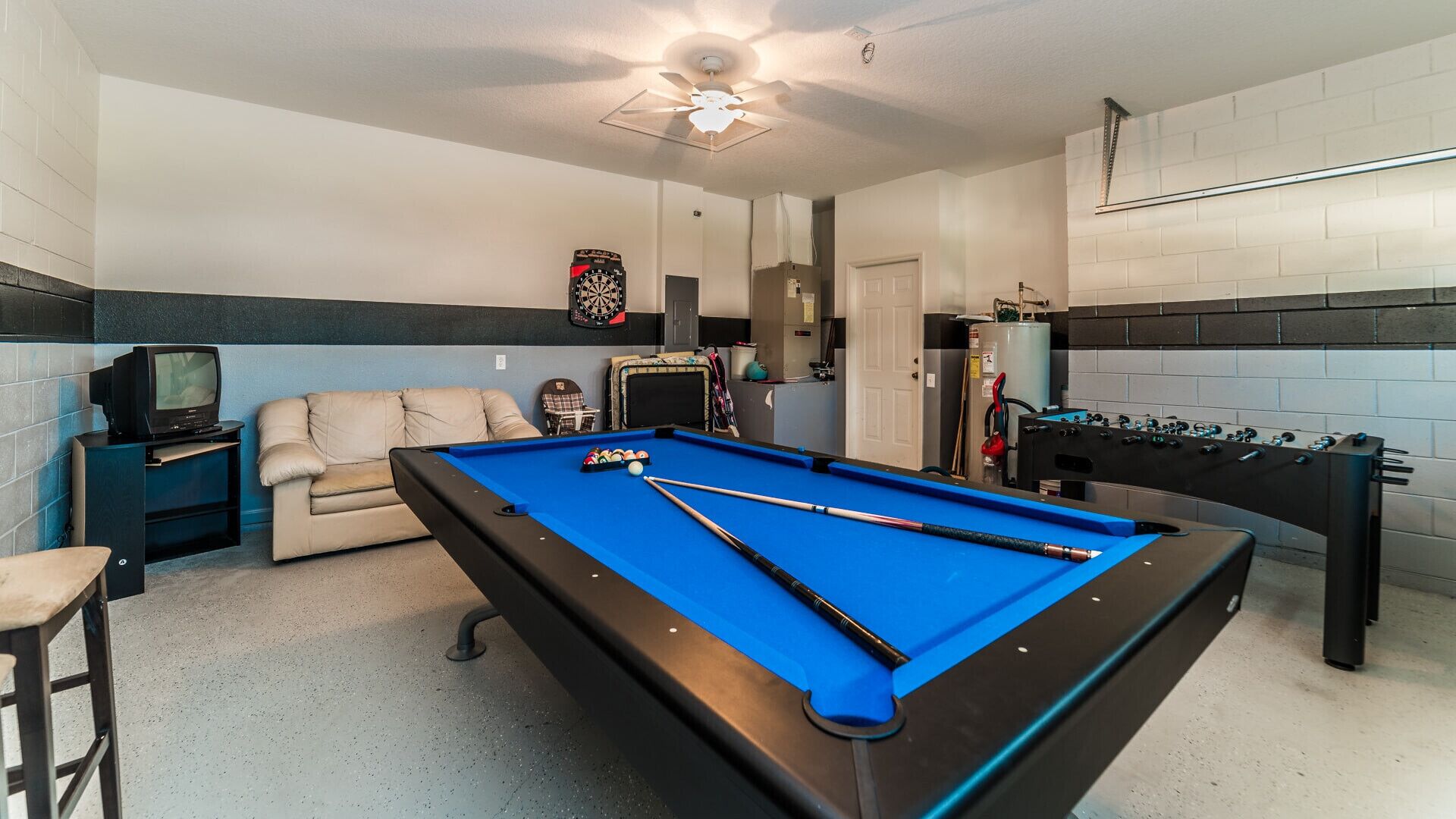 A pool table with billiard balls, a foosball table, a dartboard, and a television.