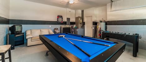 A pool table with billiard balls, a foosball table, a dartboard, and a television.