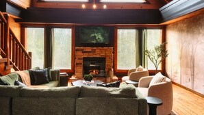 Ein gemütliches Blockhaus-Interieur mit einer Holztreppe, einem grünen Sofa, einem Kamin und einem Fernseher.