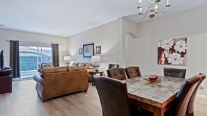 Ein geräumiges Wohnzimmer mit einer großen Couch, einem Esstisch mit Stühlen, einem Fernseher und Bildern an den Wänden.