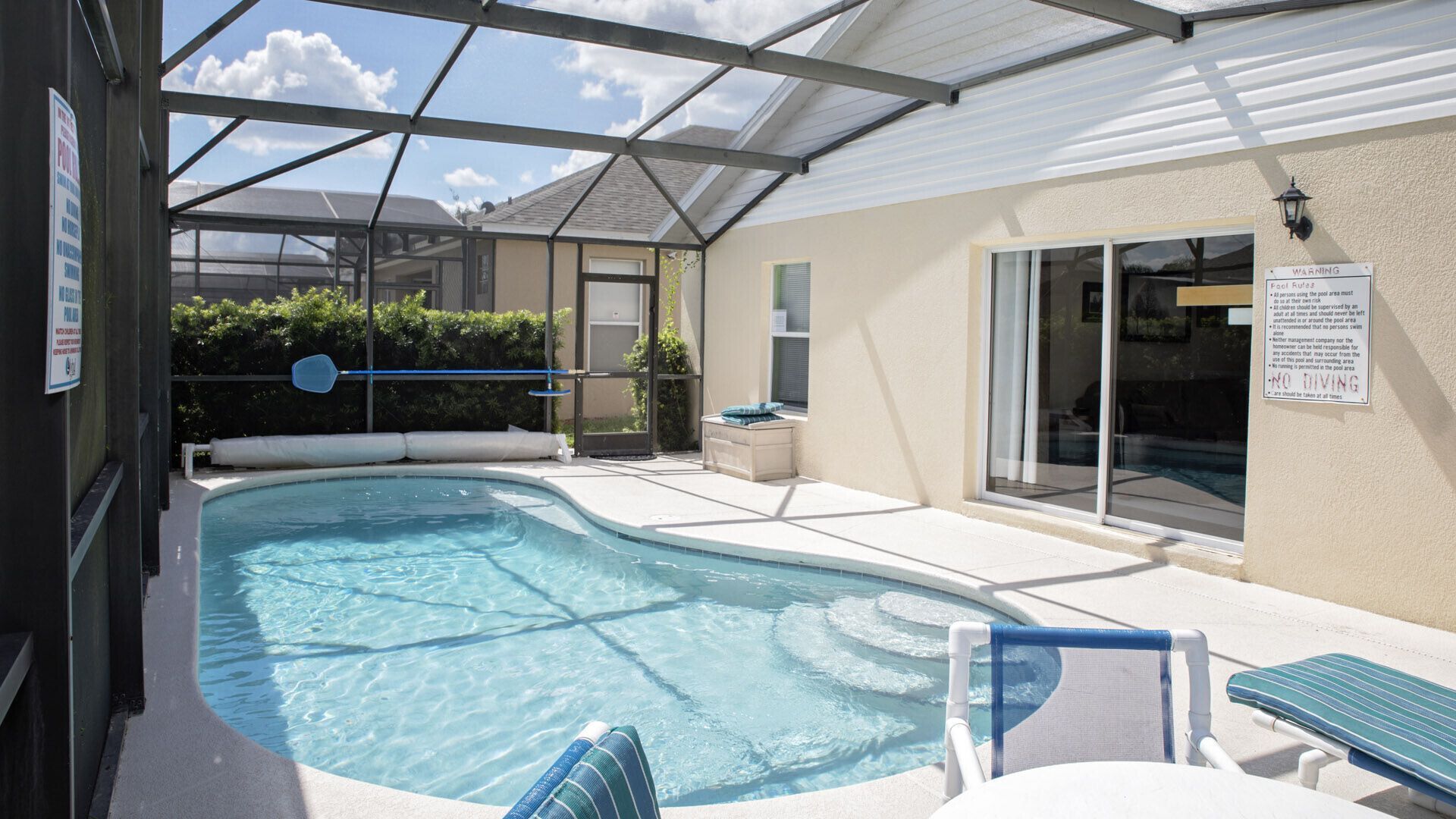 A swimming pool with a glass enclosure, lounge chairs, and a warning sign.