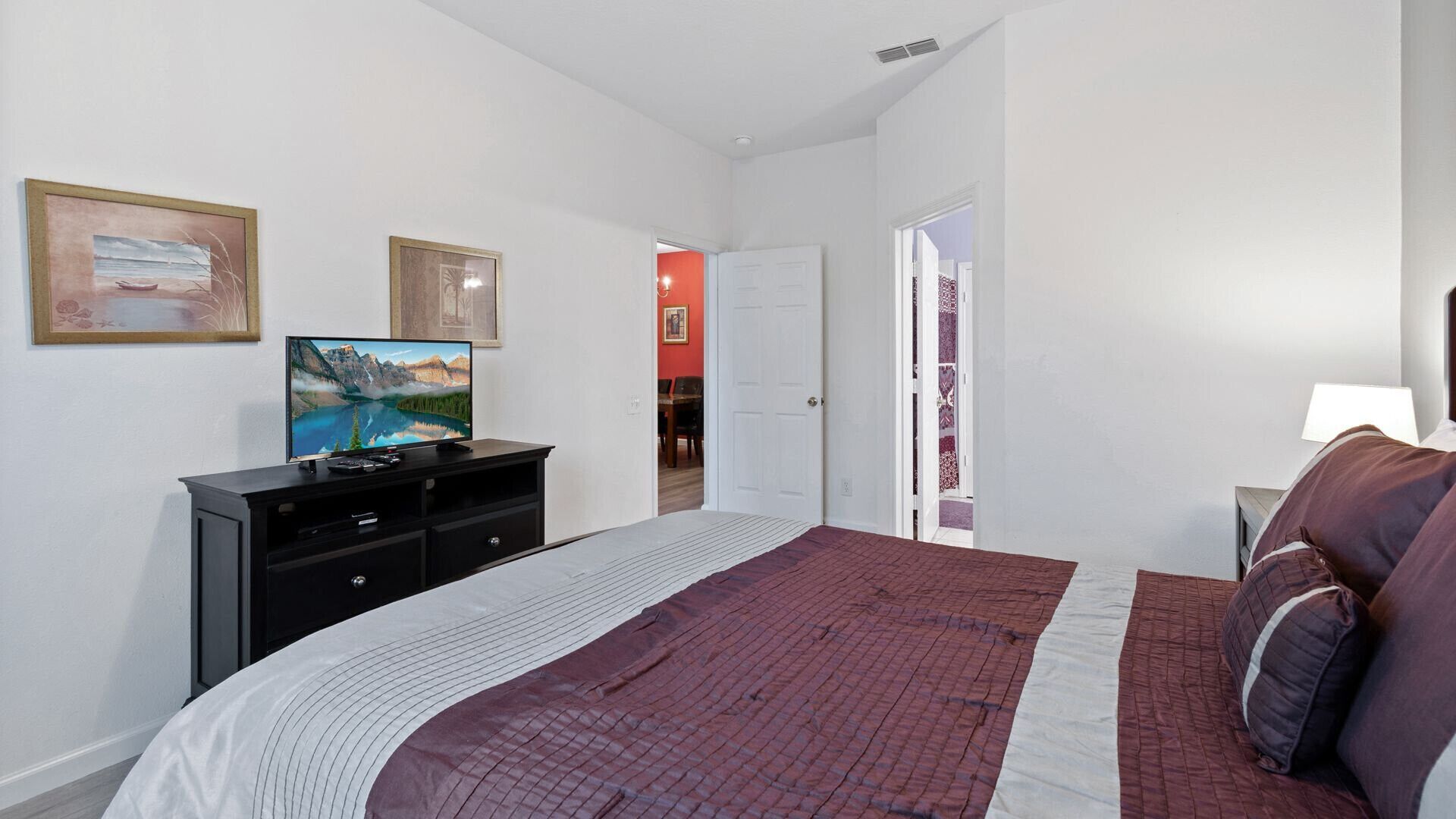 A bedroom with a bed, a TV on a dresser, and a door leading to another room.