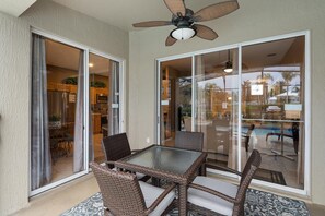A patio area with a glass table and wicker chairs, a ceiling fan, and a view of a pool and outdoor area. - Windsor Palms 75 - Four Bedroom Villa, Sleeps 10 (Orlando)