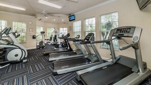 Un gimnasio con cintas de correr, elípticas y una pantalla de televisión.