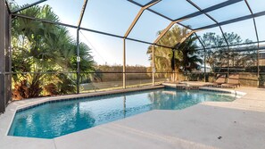 Una piscina interior con cerramiento de vidrio, rodeada de palmeras y un cielo despejado.