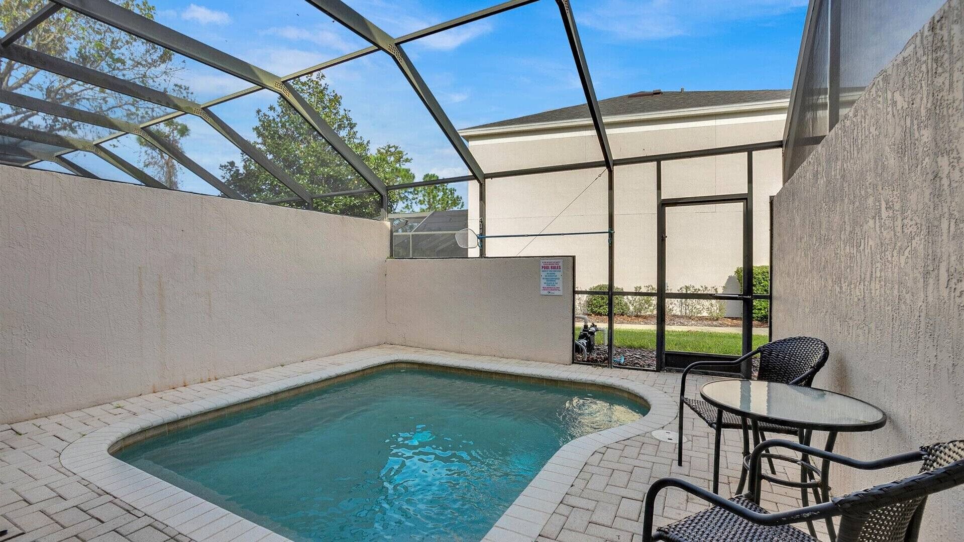 A pool area with a hot tub, a table, and chairs, surrounded by a glass enclosure.