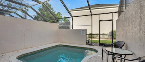 Un espace piscine doté d’un jacuzzi, d’une table et de chaises, le tout entouré d’une paroi en verre.