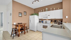 Eine moderne Küche mit weißen Geräten, einem Esstisch mit Stühlen und einem kleinen Kühlschrank.