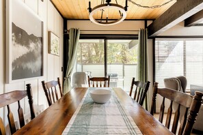A dining room with a wooden table, chairs, a chandelier, and artwork on the walls. - Premier Townhouse, Closest to the Slopes (Big Bear Lake)