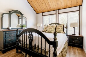 A bedroom with a wooden ceiling, a bed with a headboard, a dresser, a nightstand, and a window with blinds. - Premier Townhouse, Closest to the Slopes (Big Bear Lake)
