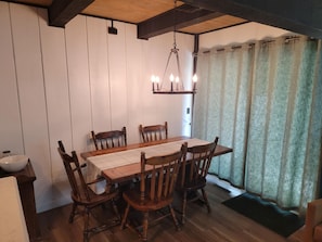 Ein Essbereich mit Holztisch und Stühlen, einer Hängelampe und Blick durch ein mit Vorhängen drapiertes Fenster.