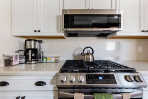 A kitchen with a stainless steel stove, a microwave, and various appliances and containers on the counter. - Premier Townhouse, Closest to the Slopes (Big Bear Lake)