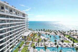Un hotel con diversi piani, una zona piscina con lettini e vista sull'oceano.