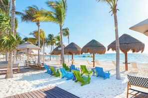 Una spiaggia con ombrelloni di paglia, palme e comode sedie da spiaggia colorate.