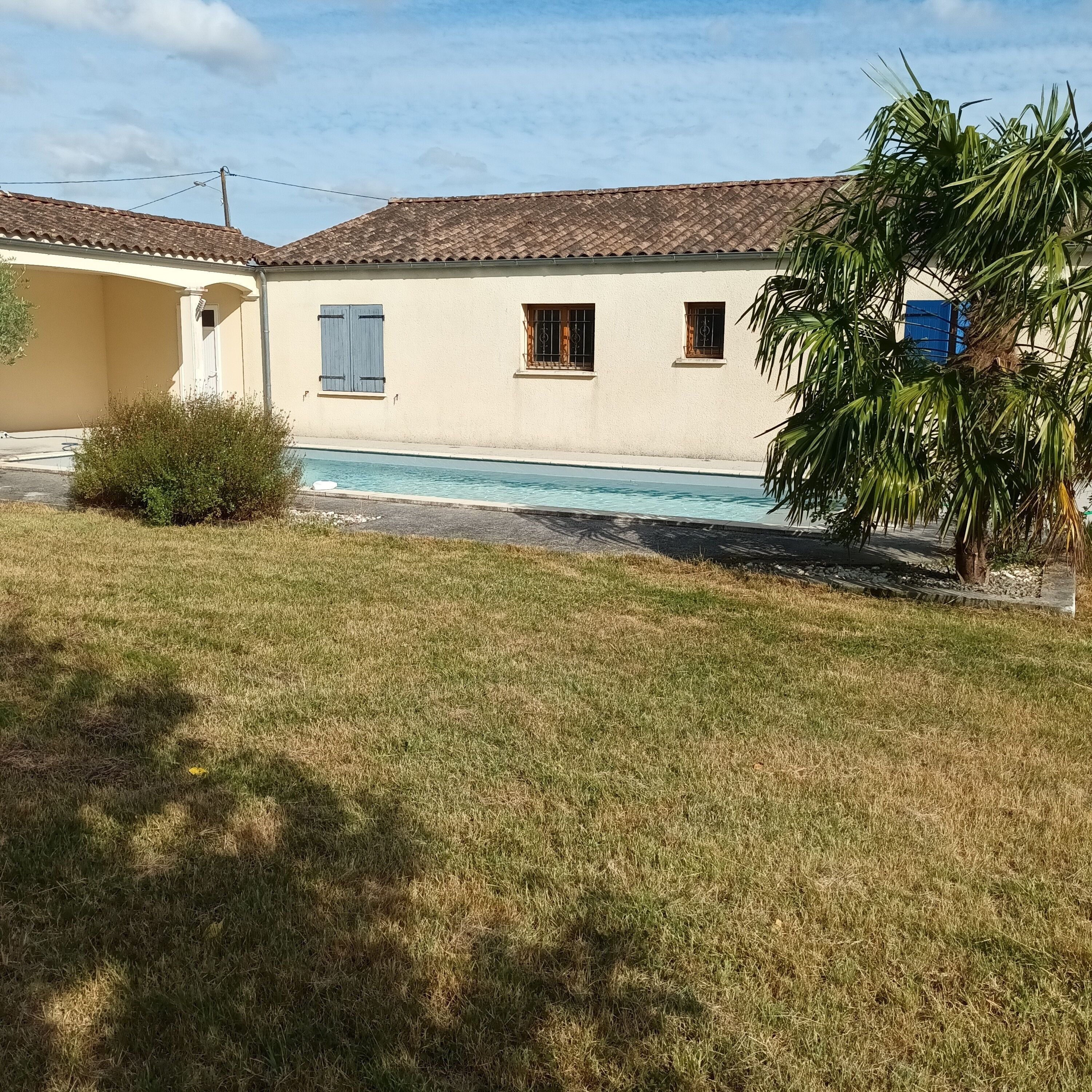 A residential property with a swimming pool, a lawn, and a building with a tiled roof.