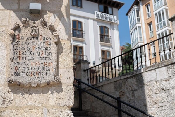Una placa de piedra con texto histórico, una escalera con barandilla metálica y un edificio con un letrero que dice 'HOTEL'.