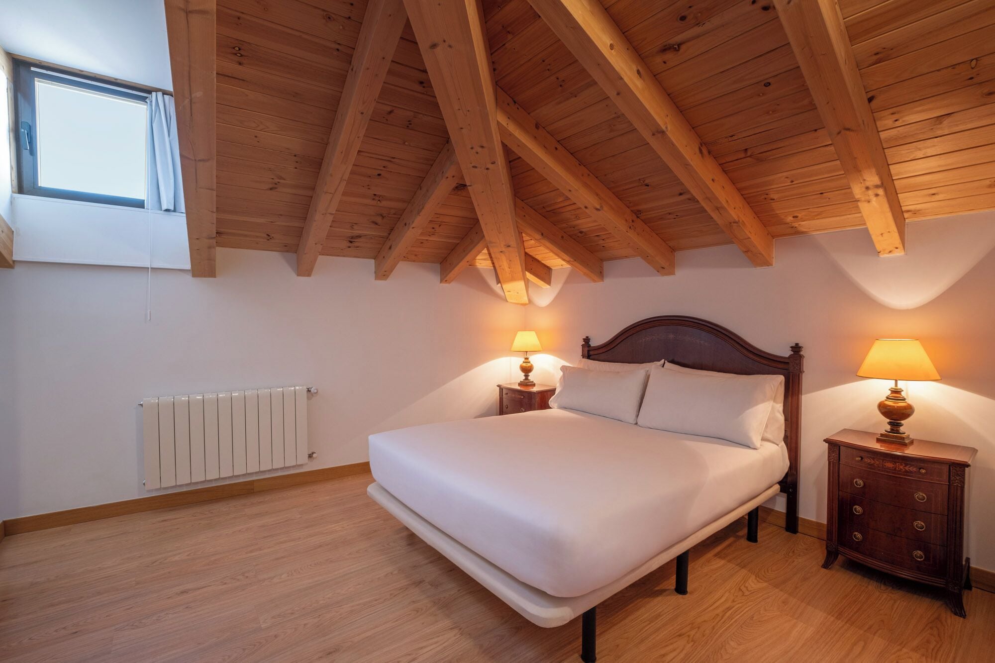 Une chambre avec un plafond en bois, un lit, des tables de chevet et une fenêtre.