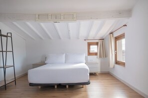A bedroom with a bed, a nightstand, a window with curtains, and a wooden floor.