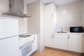 A compact kitchen with white cabinetry, a stainless steel range hood, a built-in oven, a microwave, and a sink.