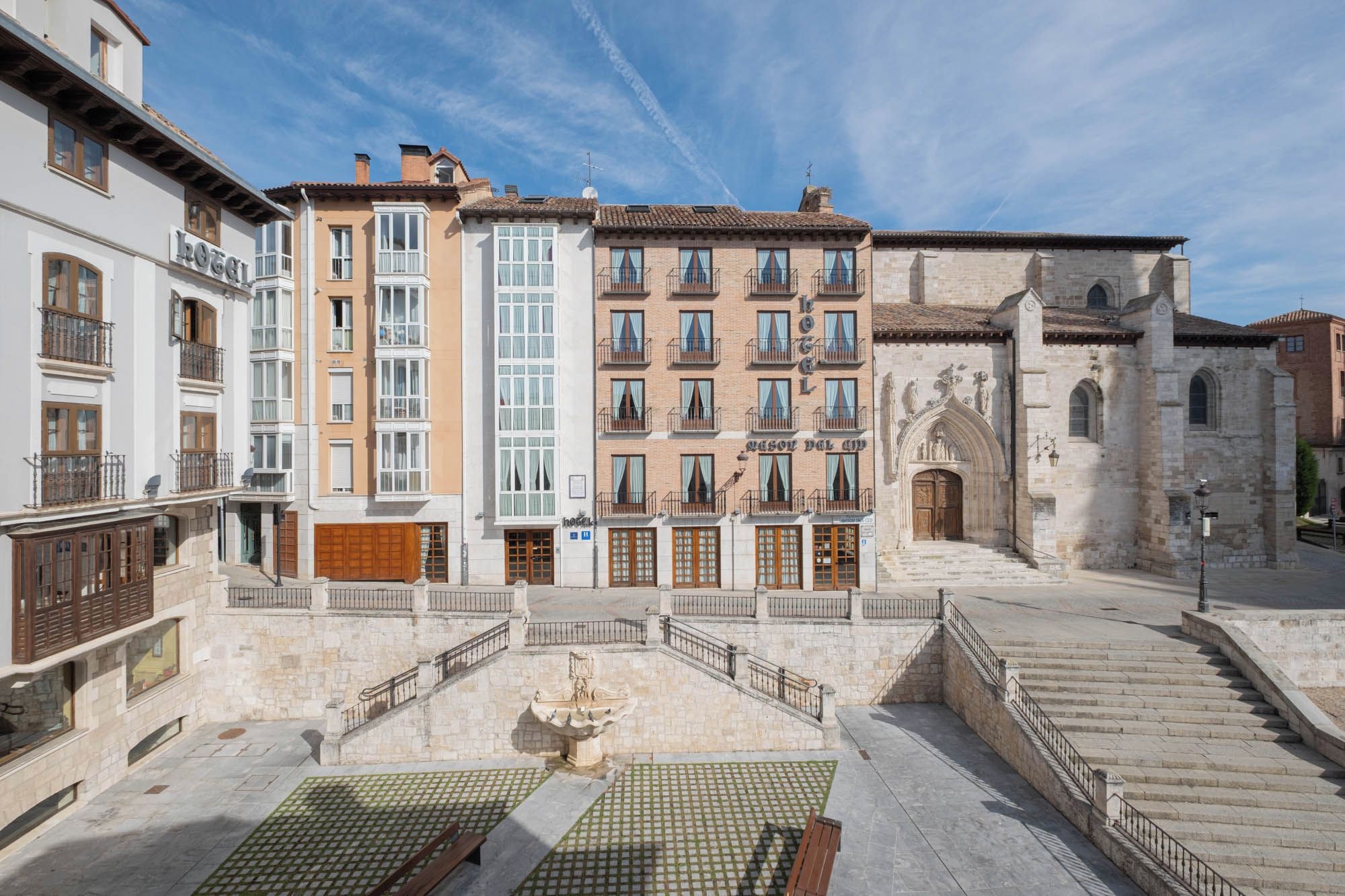 A hotel with multiple floors, a courtyard with a fountain, and a church in the background.