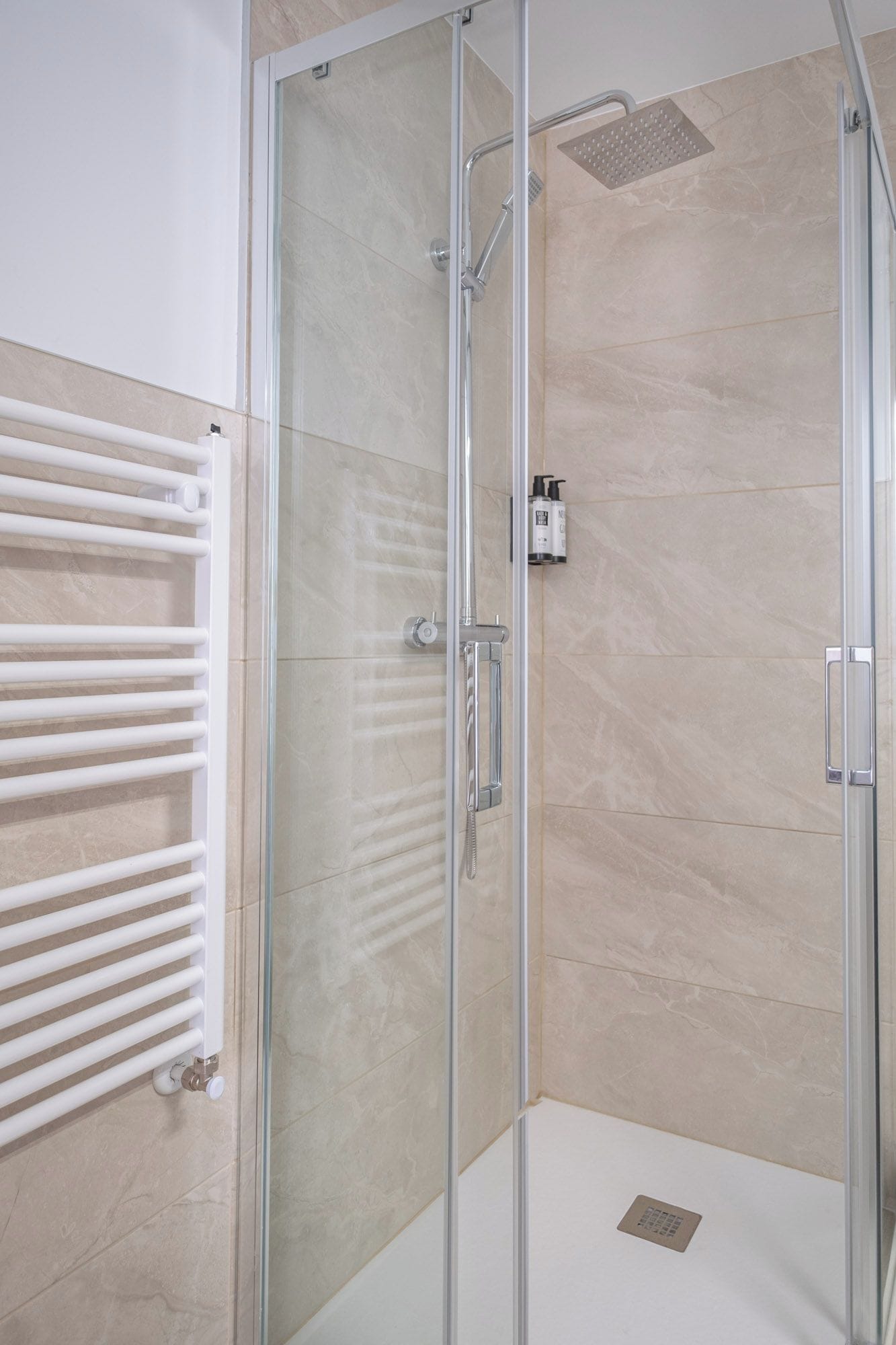 A glass-enclosed shower with a handheld showerhead and a wall-mounted control panel.