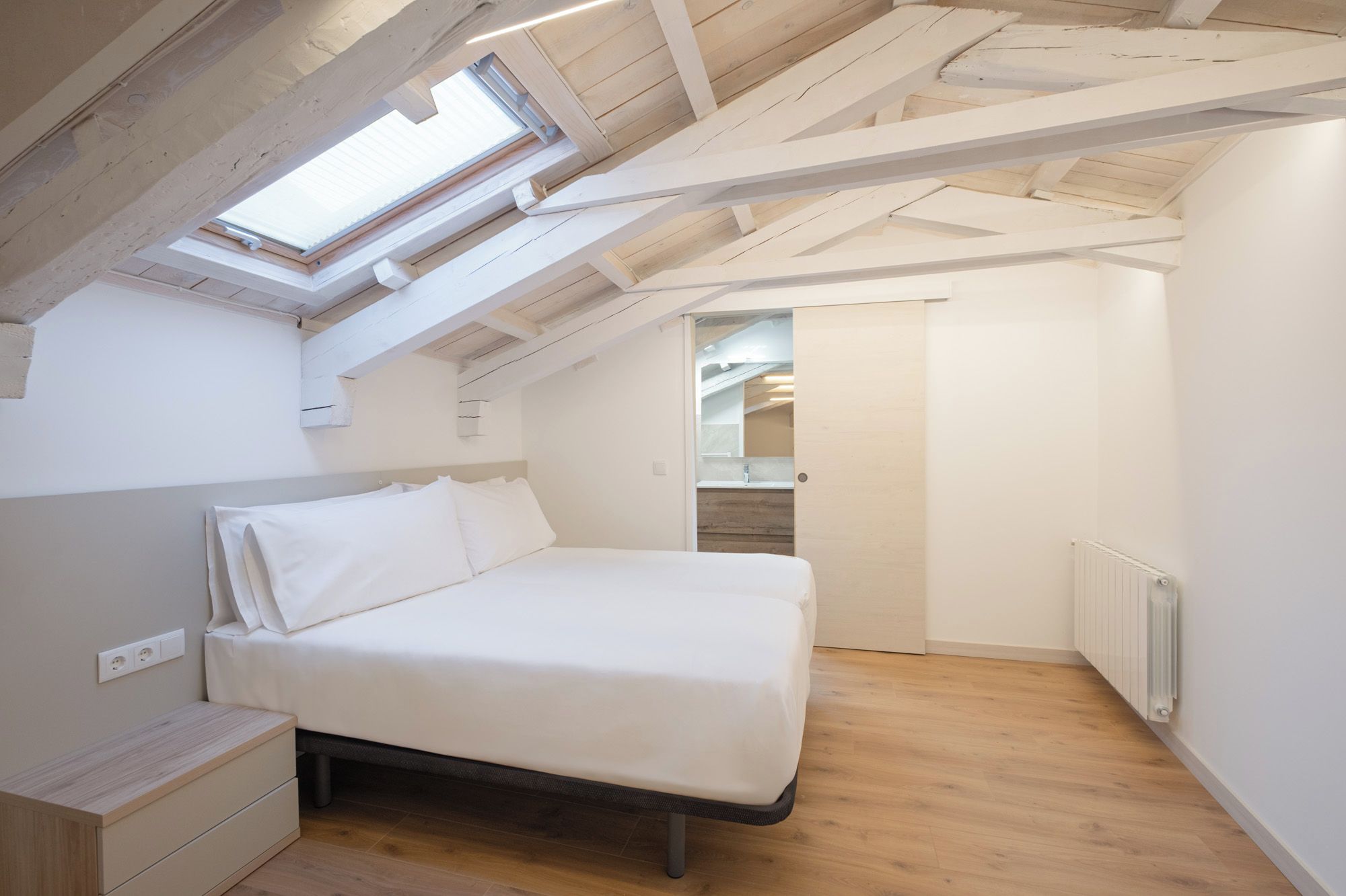 Een slaapkamer met een schuine kap, dakraam, bed, nachtkastje en een inloopkast.